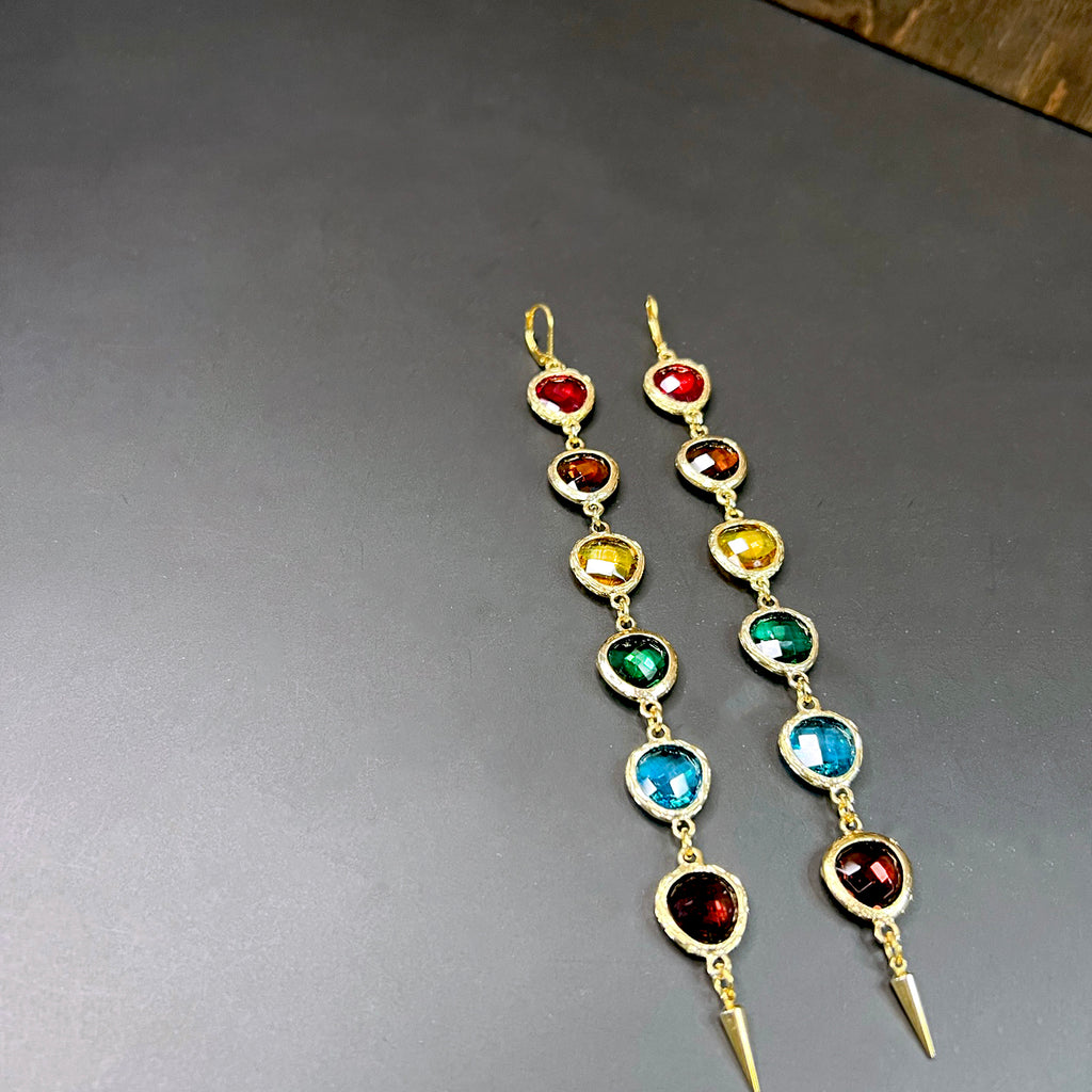 Angled view of linear rainbow crystal earrings with gold hardware and pointed tips – bold colorful statement earrings