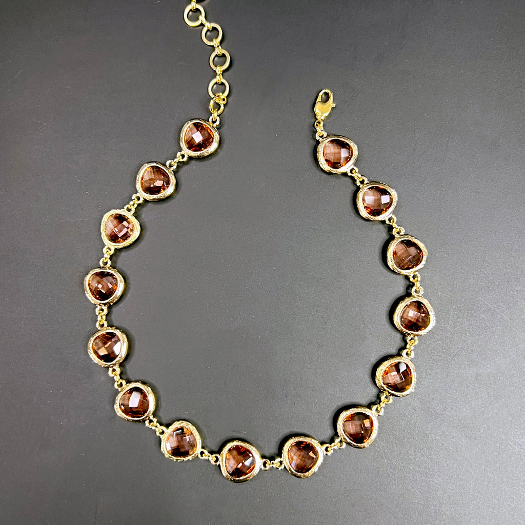 Choker necklace with soft blush pink faceted stones set in hammered gold-tone bezels, displayed in a curved shape against a black background.