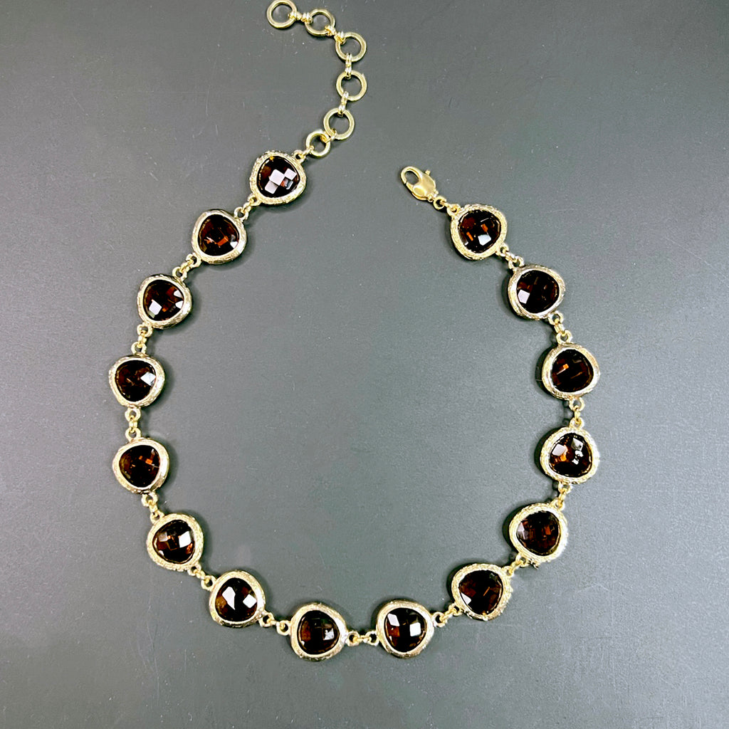 Close-up of a burnt orange crystal choker with faceted stones linked in gold-tone bezels, shown in an elegant arc on a black surface.