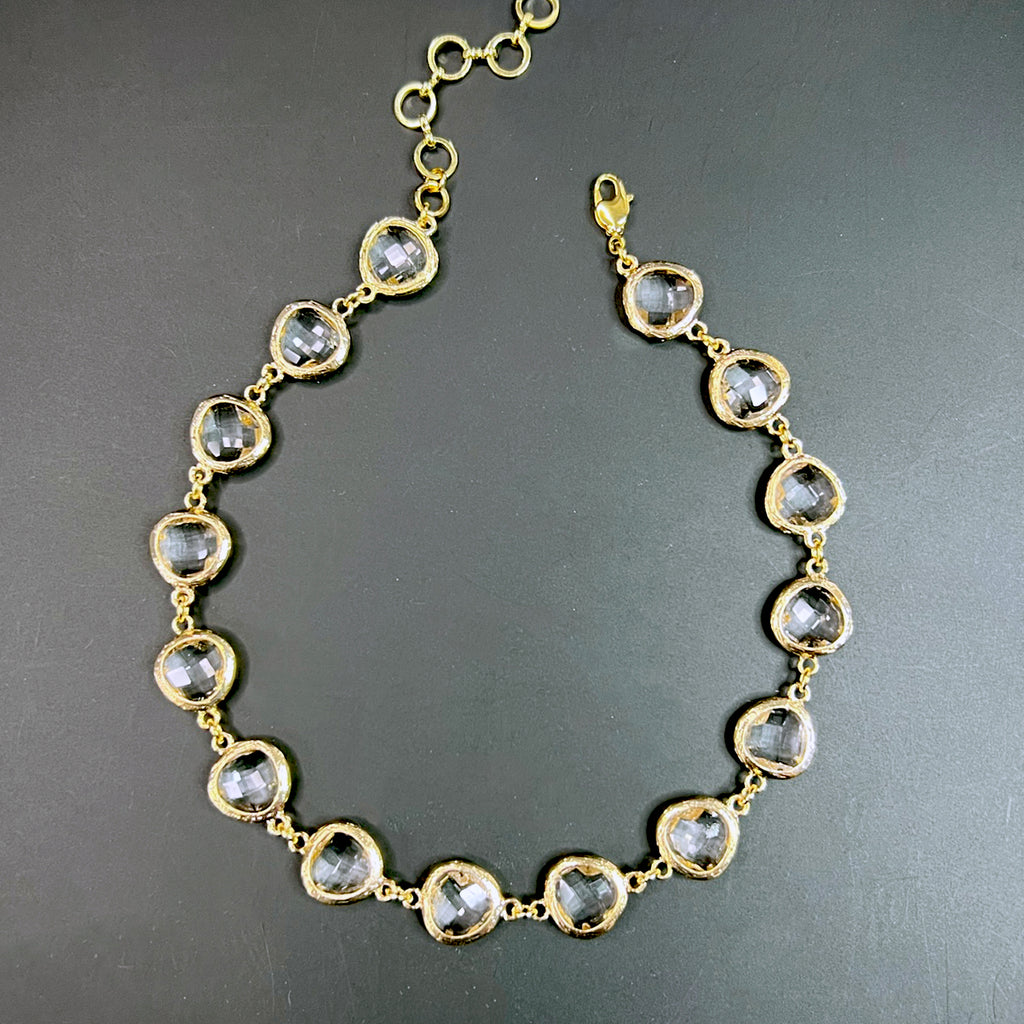 Clear crystal choker necklace with faceted transparent gems set in irregular textured gold-tone bezels, arranged on a flat black background.