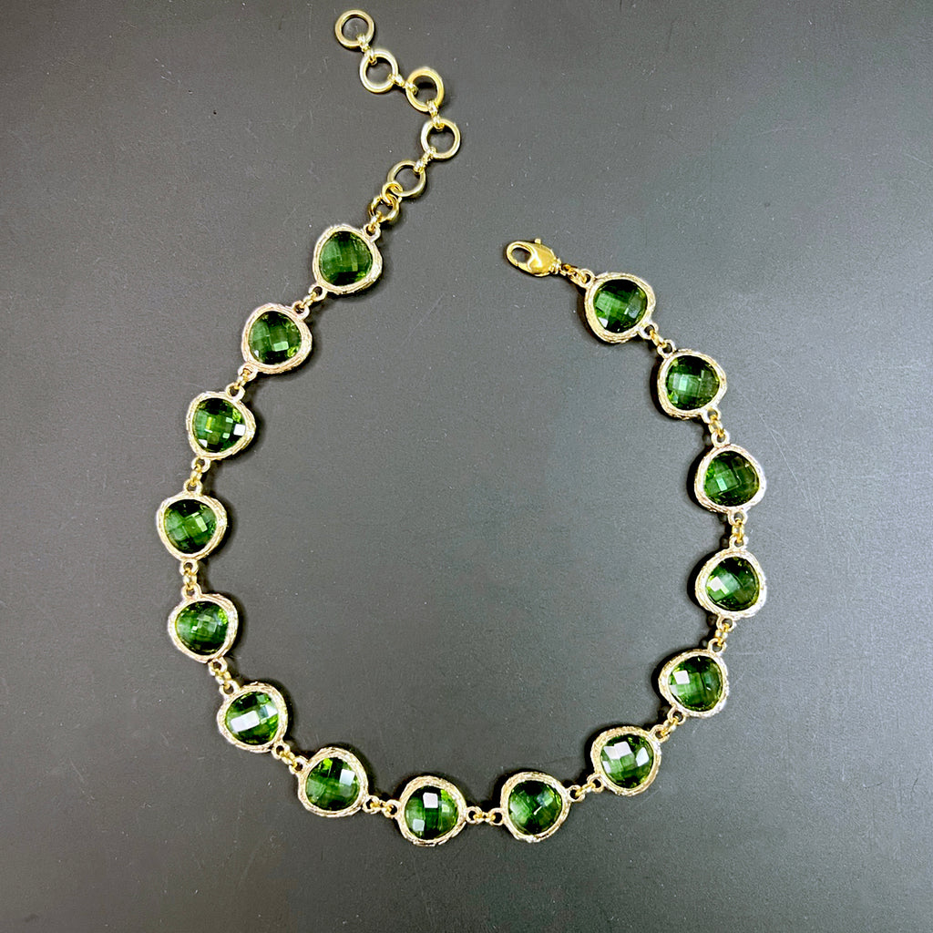 Olive green crystal choker necklace featuring faceted stones in hammered gold settings, laid out in a symmetrical semi-circle on a black background.