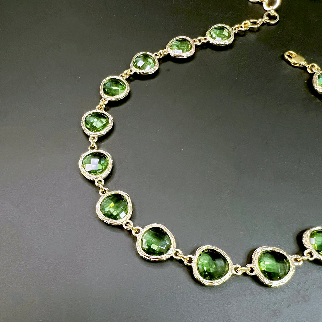 Olive green crystal choker necklace featuring faceted stones in hammered gold settings, laid out in a symmetrical semi-circle on a black background.
