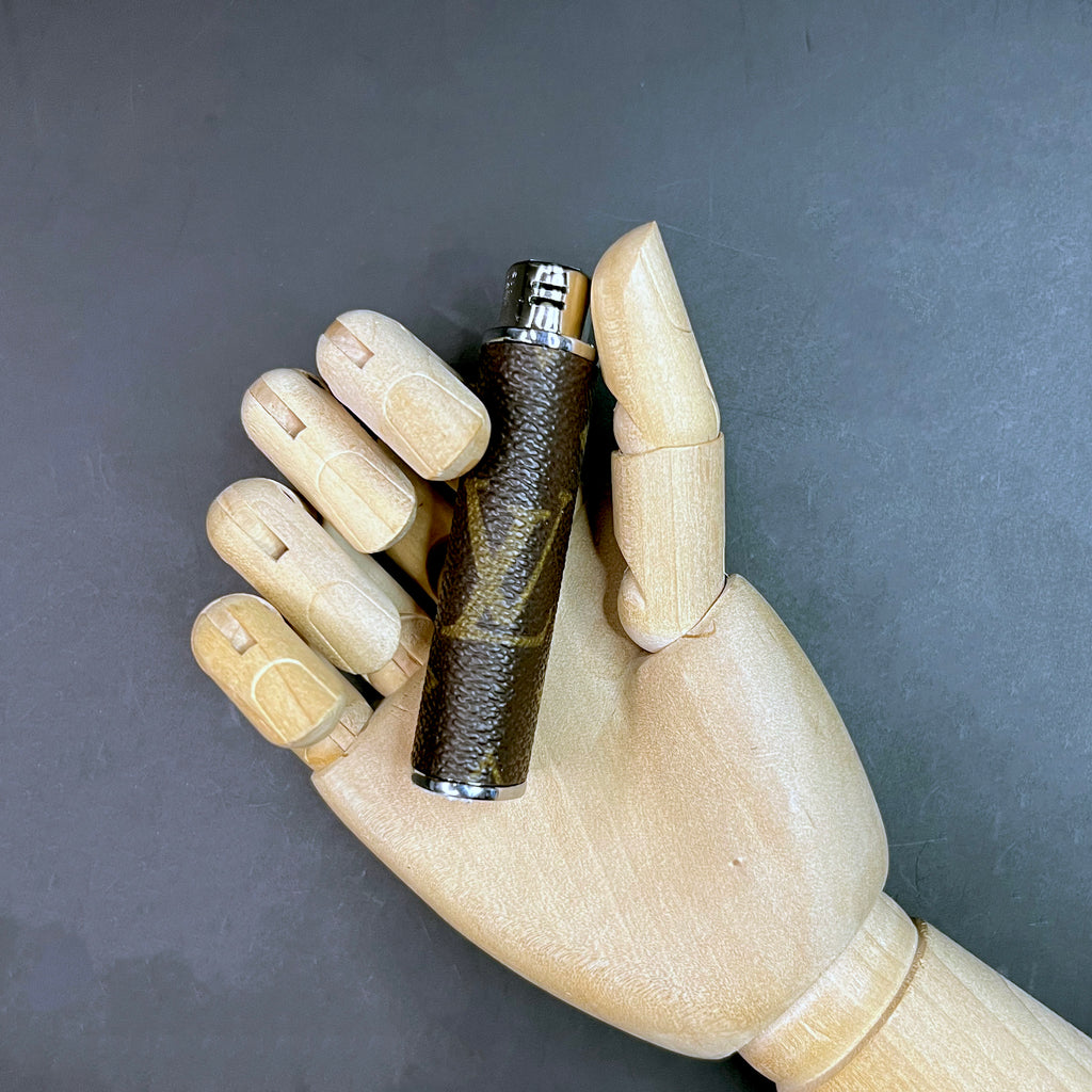 Hand holding a luxury lighter case wrapped in classic Louis Vuitton monogram canvas.