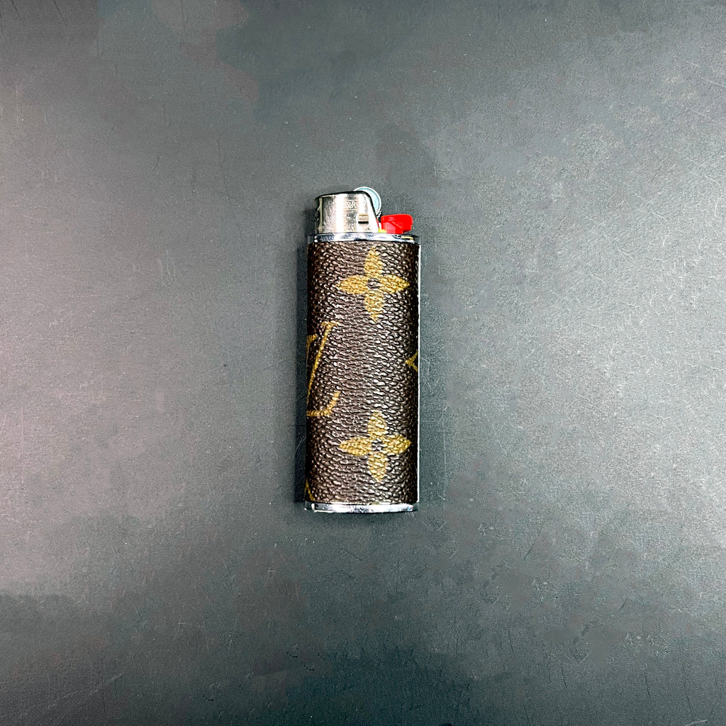 Close-up of a Louis Vuitton monogram lighter case with silver hardware on a dark background.