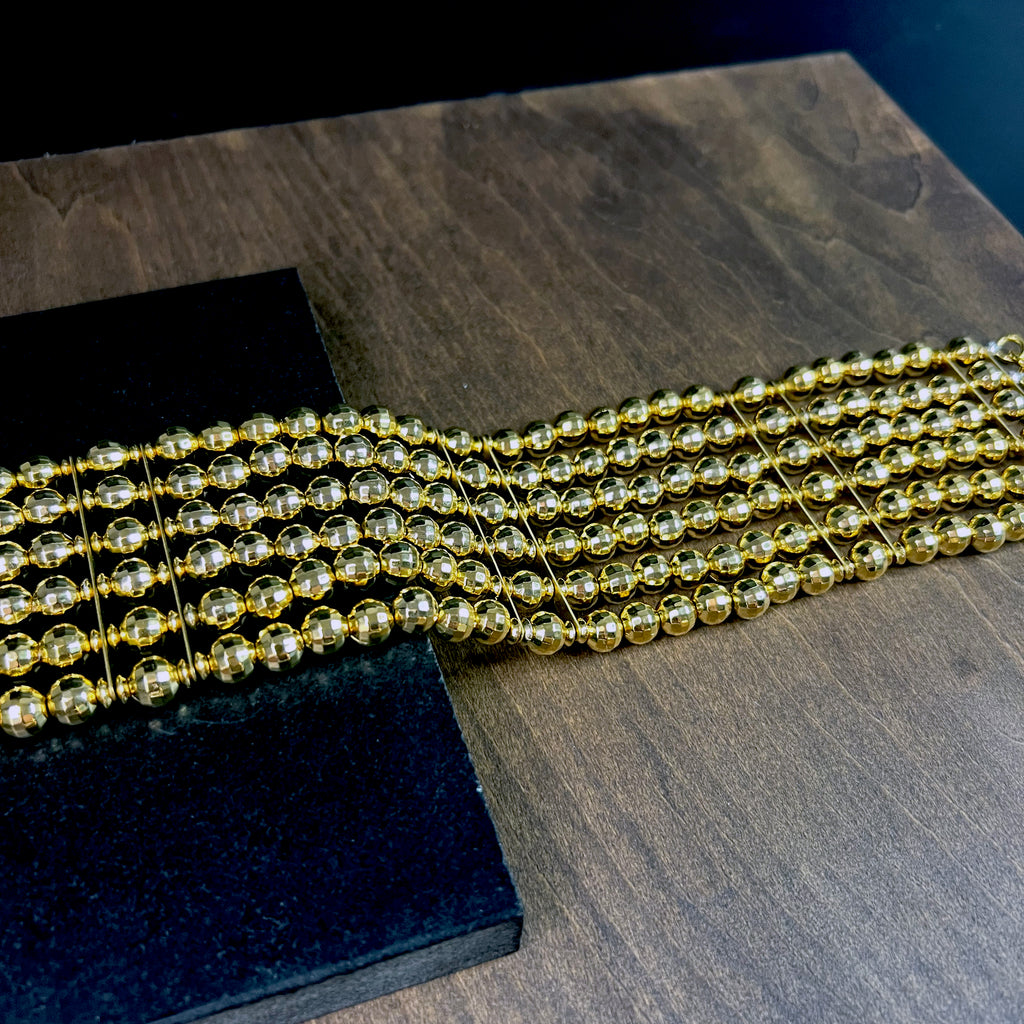 Angled detail of sculptural gold beaded choker on wood – reflective faceted statement necklace