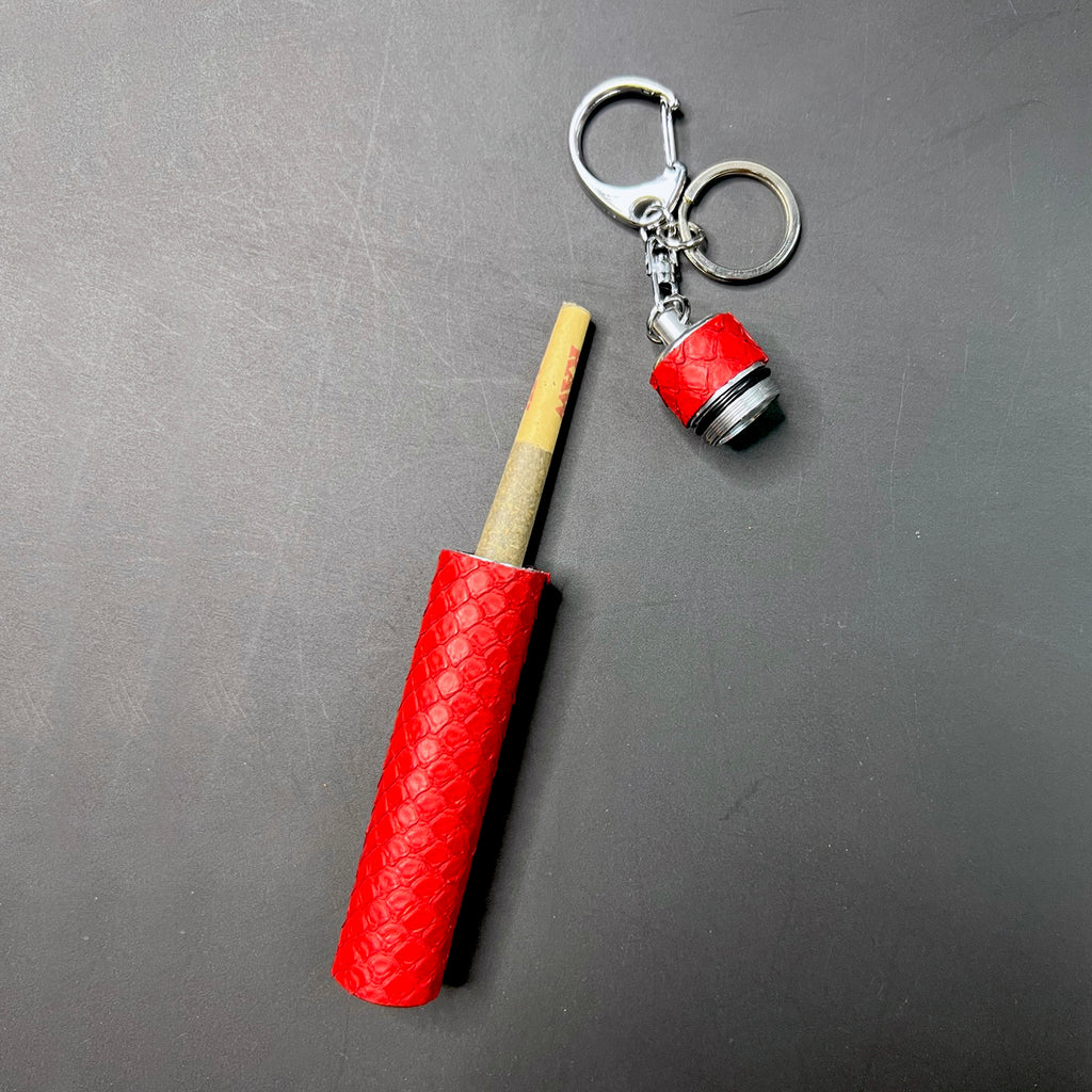 Fashionable red python pre-roll holder opened to reveal joint, featuring silver keychain hardware