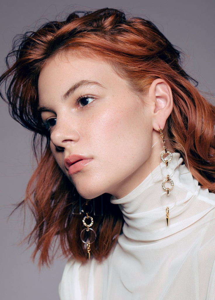 Modern acrylic and gold earrings with layered drop design and spiked pendant detail styled on model with messy hair and white sheer turtleneck