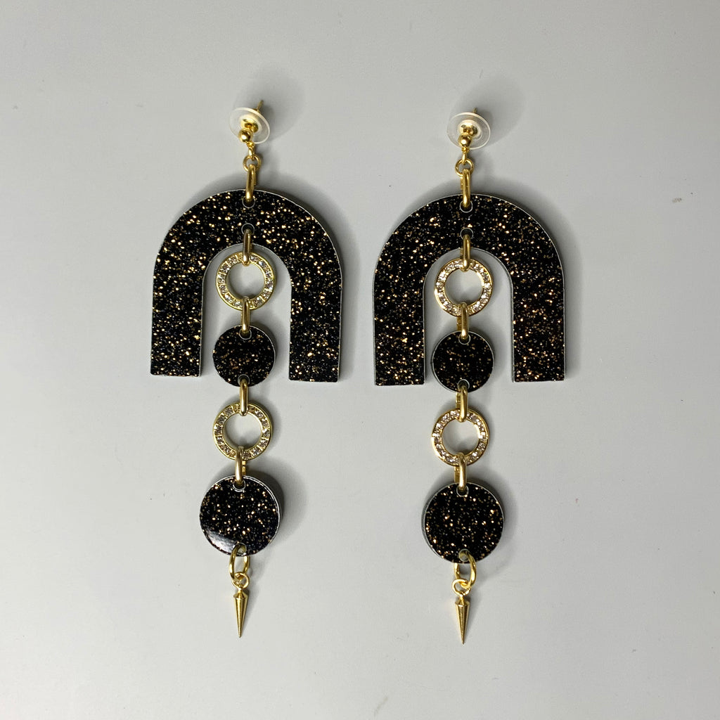 "Front view of Haus of Topper’s Disco Noir Chandelier Earrings featuring black glitter arches, crystal-studded rings, and gold spike drops on a gray background"
