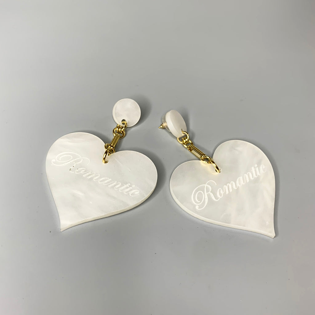 Close-up of white Romantic Heart Statement Earrings featuring bold heart shapes and gold chain links