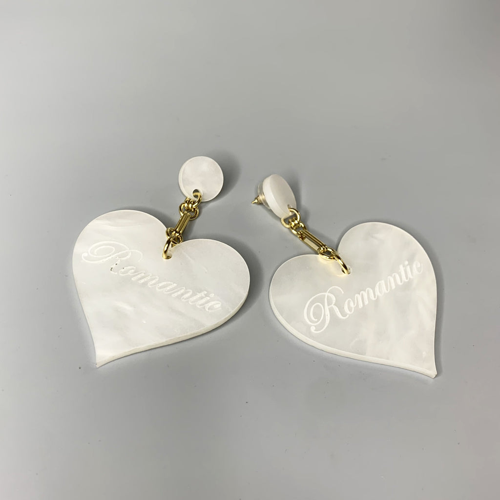 Lightweight white acrylic heart earrings with gold chain and romantic script detail on wood background