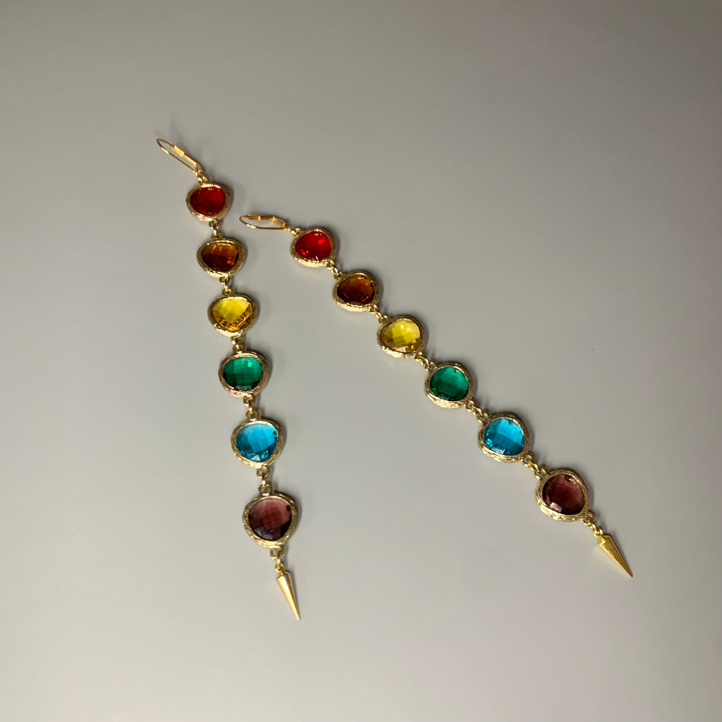 Angled view of linear rainbow crystal earrings with gold hardware and pointed tips – bold colorful statement earrings