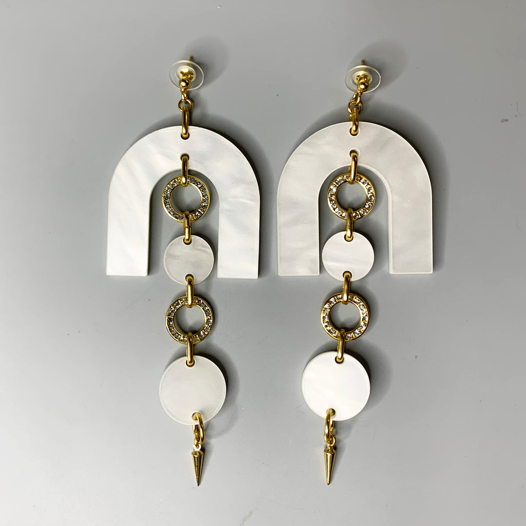 Pearlized white acrylic statement earrings with arched top, gold crystal rings, and spike drop