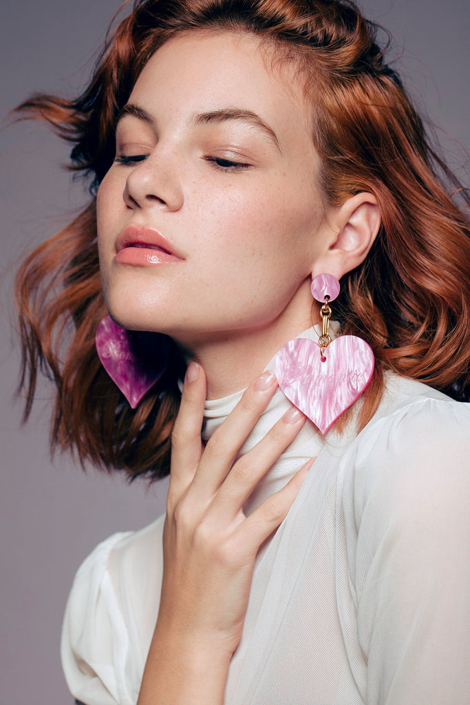 Model wearing oversized pink Romantic Heart Statement Earrings with white turtleneck for a chic fashion-forward look