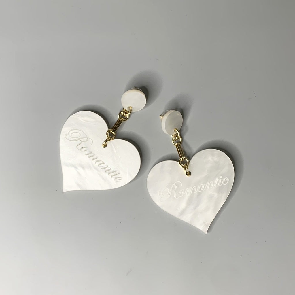 Close-up of white Romantic Heart Statement Earrings featuring bold heart shapes and gold chain links