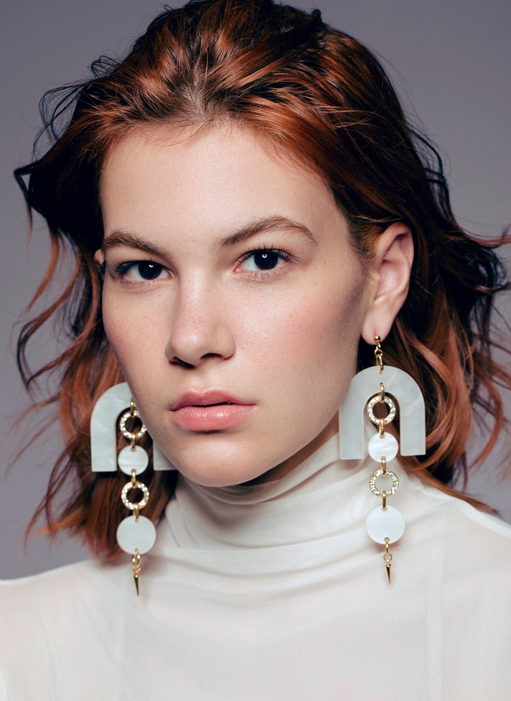 Model wearing bold pearlized white acrylic earrings with crystal gold rings and spiked drop – statement earrings