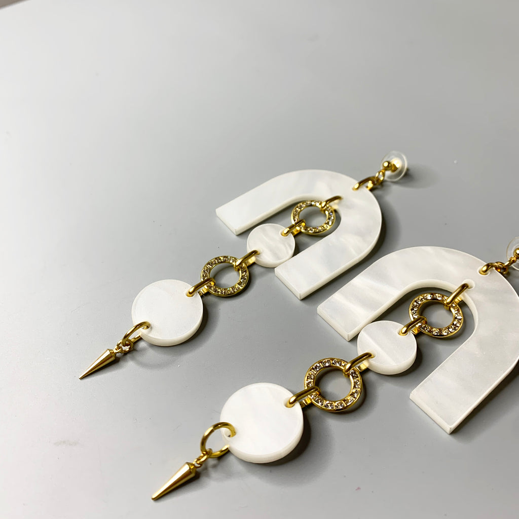 Detail side view of sculptural pearl acrylic earrings with gold accents and layered drop design