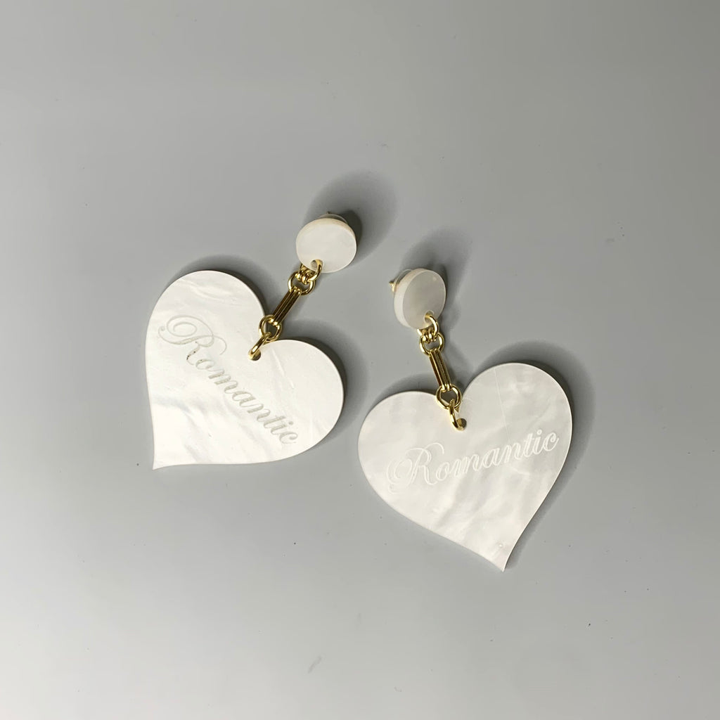 Lightweight white acrylic heart earrings with gold chain and romantic script detail on grey background