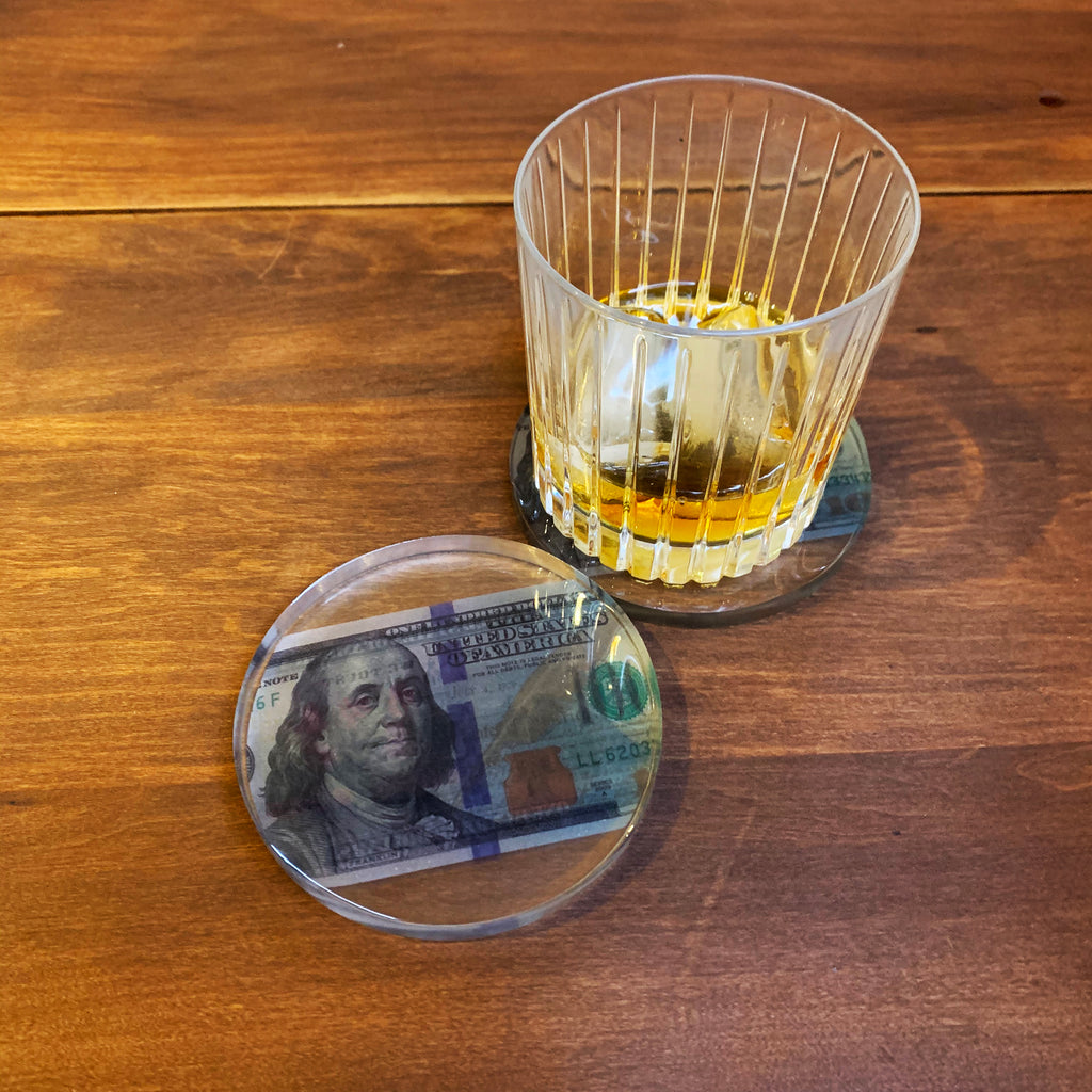 Still life image of clear resin coaster with one hundred dollar bill inside