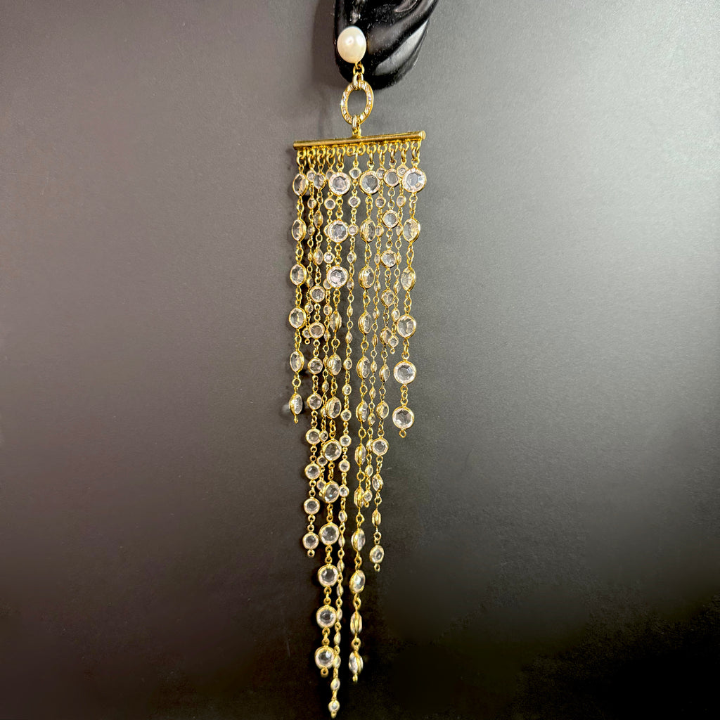 Side angle of the long gold crystal fringe earring on a display ear, showing movement and sparkle of the cascading crystal chains.