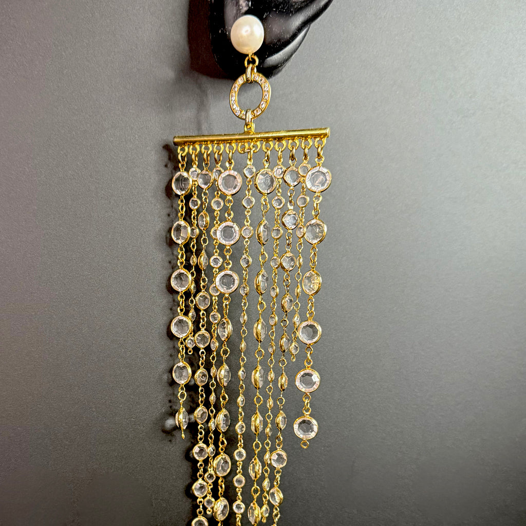 Single long gold crystal fringe earring hanging from a black display ear, featuring a pearl stud and cascading clear crystal chains.
