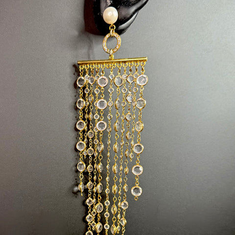 Single long gold crystal fringe earring hanging from a black display ear, featuring a pearl stud and cascading clear crystal chains.
