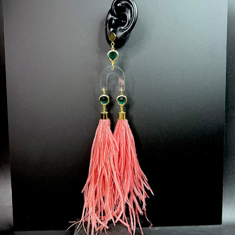 Bold pink feather earrings with clear acrylic arch, emerald green gemstones, and gold-tone accents