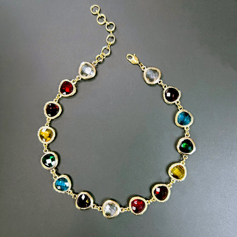 Gold choker necklace with vibrant rainbow-colored crystals arranged in a full circle, laid flat on black background