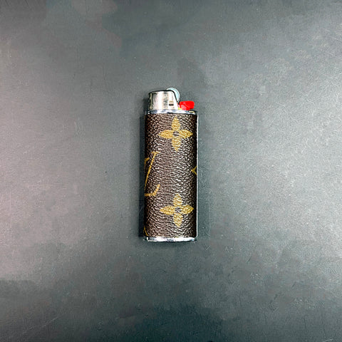 Close-up of a Louis Vuitton monogram lighter case with silver hardware on a dark background.