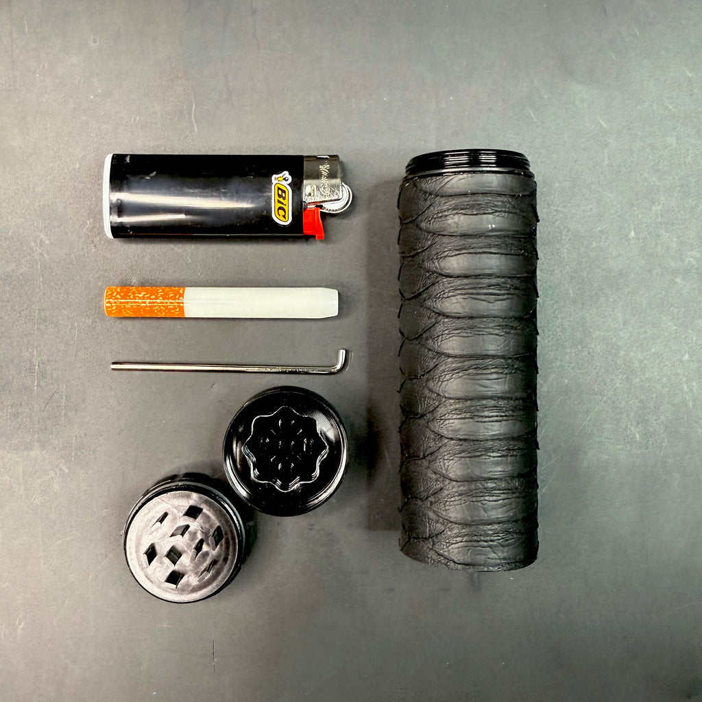 Disassembled Matte Black Python Dugout with all components laid out — matte python case, grinder top and bottom, black lighter, one-hitter, and metal poker tool arranged on a dark surface.