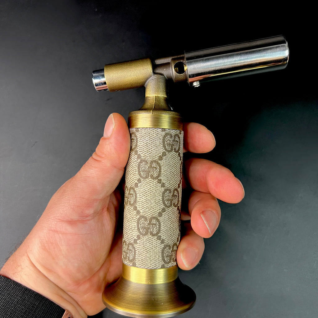Hand holding vintage GG wrapped brass torch, showcasing canvas texture and metallic finish.