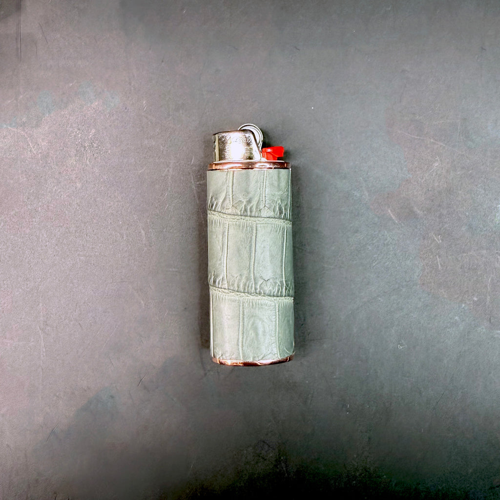 Flat lay of the limited edition grey croc lighter case on a dark surface, revealing its elegant tone, natural pattern, and polished rose gold detailing.