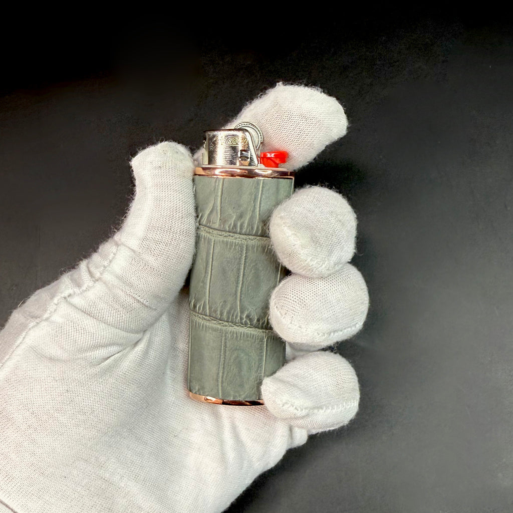 Front view of the grey croc lighter case in a gloved hand, showcasing the refined texture and rose gold metal detailing.