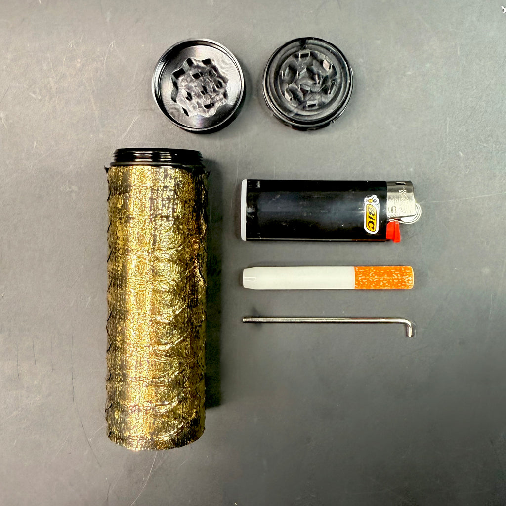 Disassembled view of the Metallic Gold Python Dugout with all components laid out — gold python-wrapped case, grinder top and bottom, lighter, one-hitter, and poker tool arranged neatly on a dark background.
