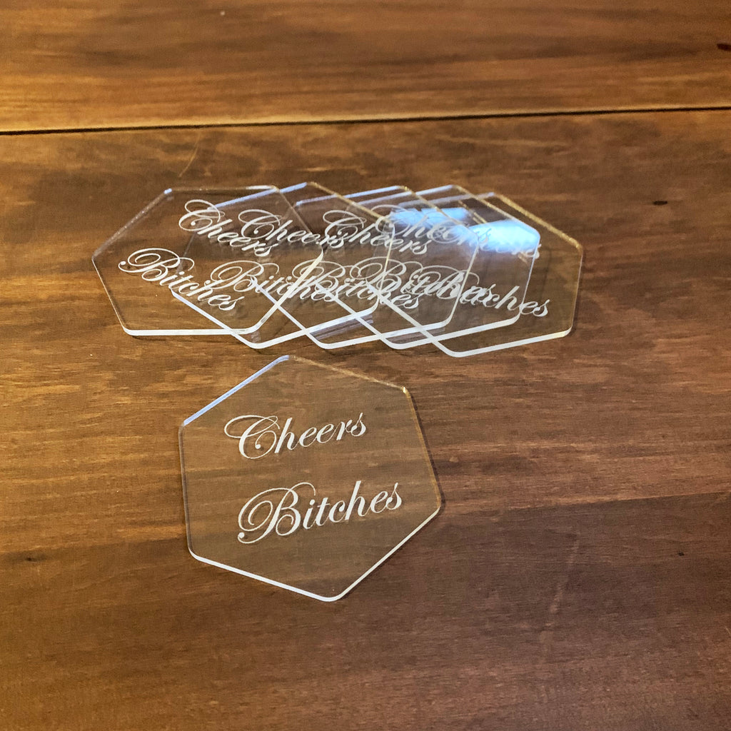 Hexagon snapped clear acrylic drink coasters with the phrase Cheers Bitches engraved on them
