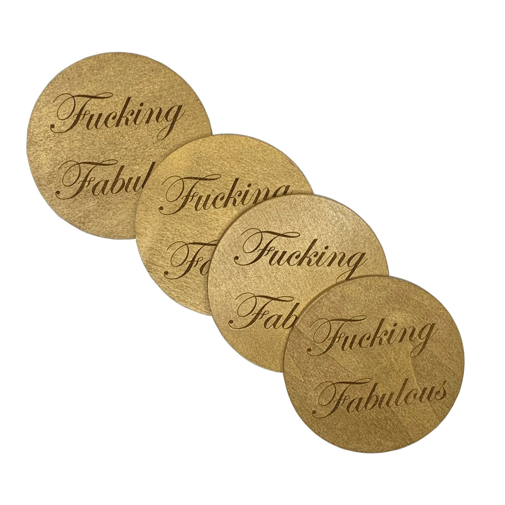 Round wood coasters coated in gold enamel and engraved with the phrase "Fucking Fabulous" in cursive