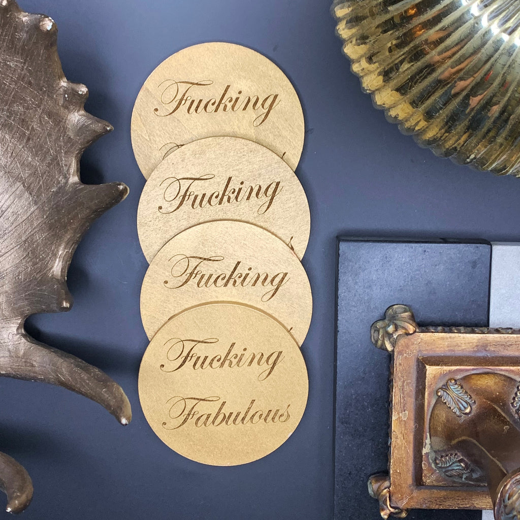 4" diameter, round wood coasters coated in gold enamel and engraved with the phrase "Fucking Fabulous" in cursive