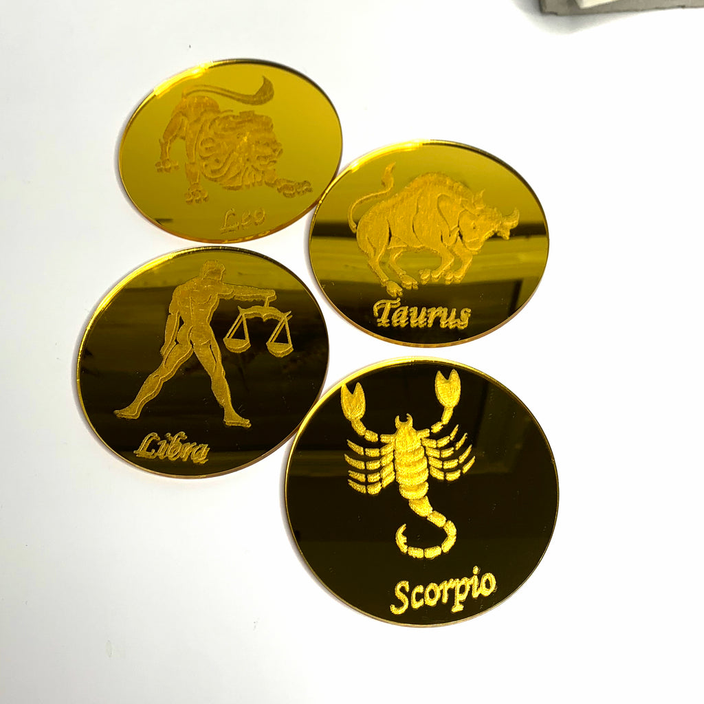Round, gold mirrored acrylic drink coasters engraved with the zodiac signs 