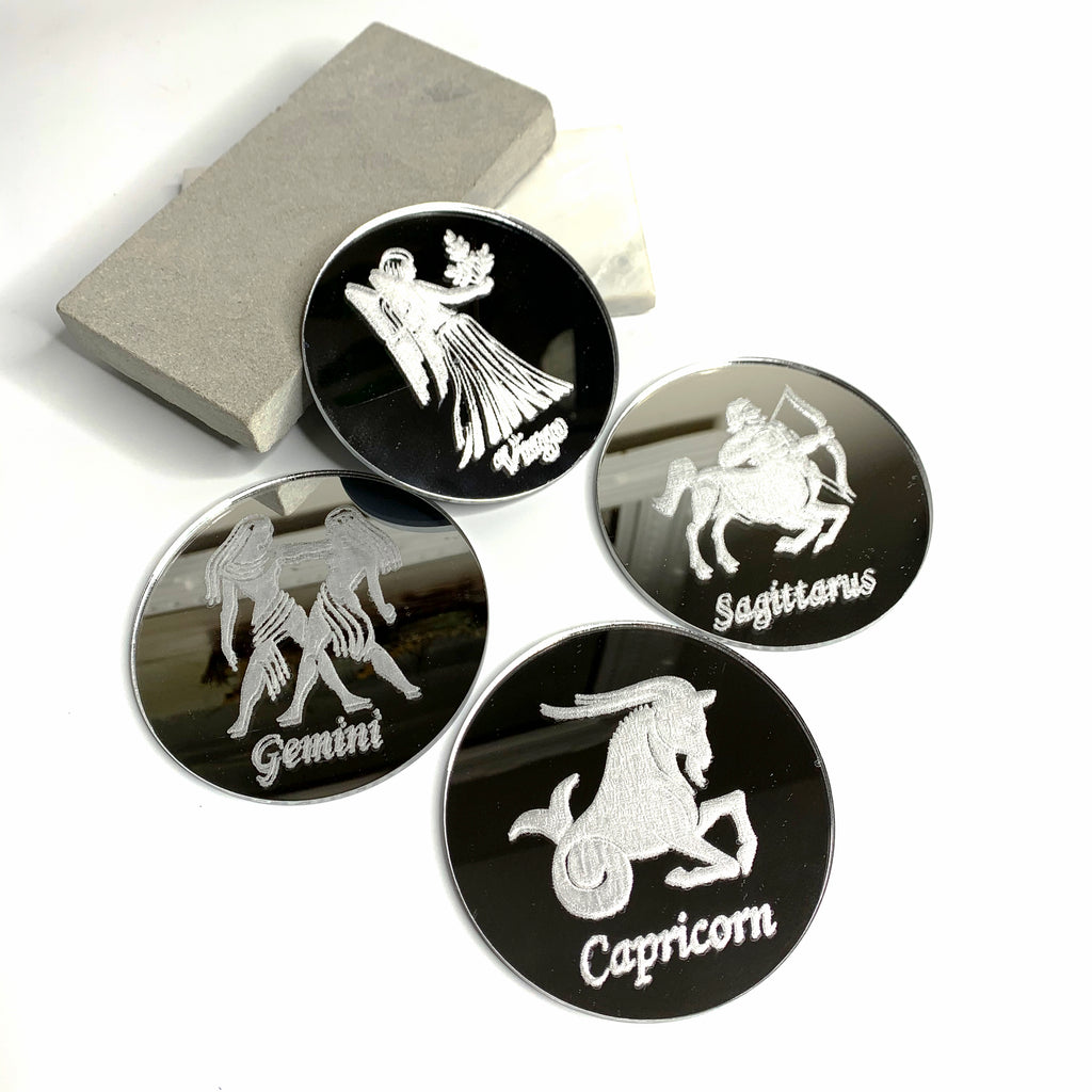 Silver mirrored, round drink coasters each engraved with a different zodiac sign